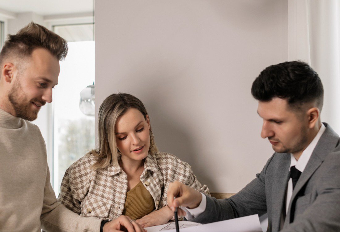A letting agent sits with a couple and points to a document as he explains the real costs of them managing properties themselves compared to hiring professional management.